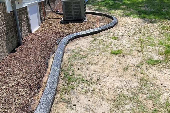 The finished charcoal stamped concrete curb following the same line around the air conditioning unit