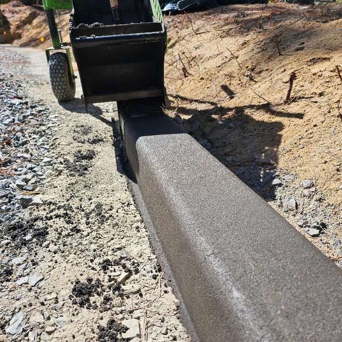 Close-up of the extruder head forming a concrete landscape curb over a prepared gravel base