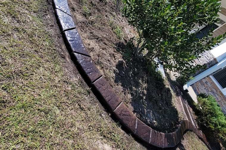 Brick-pattern concrete curb forming a tree ring around a young tree in a residential lawn