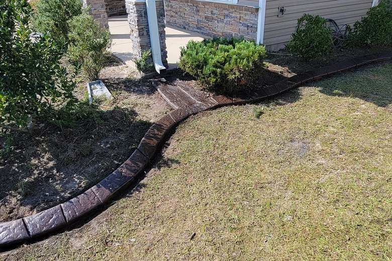 Stamped concrete curbing dividing a lawn from a planted bed against a home’s foundation