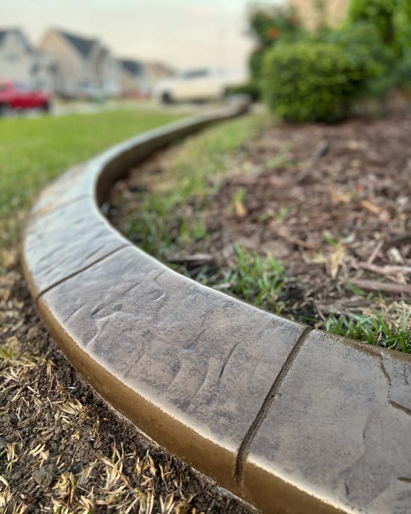 Tan and gold stamped concrete curb curving around a mulched landscape bed