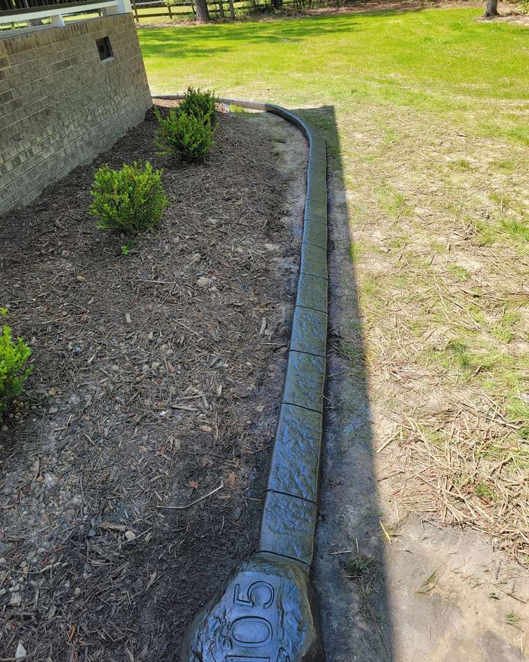 Gray concrete curb edging a planting bed along the side of a home