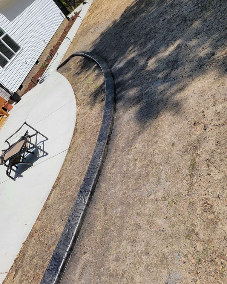 Dark concrete curb curving through a lawn beside a concrete driveway and patio