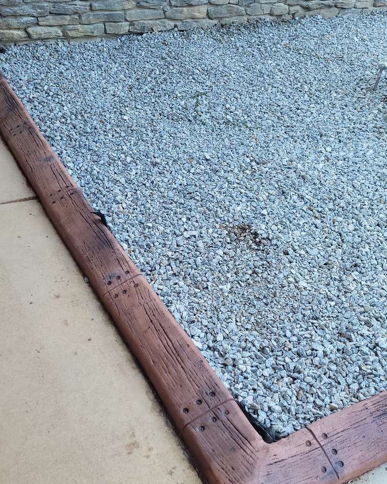 Wood-grain stamped concrete curb holding a white gravel bed beside a sidewalk