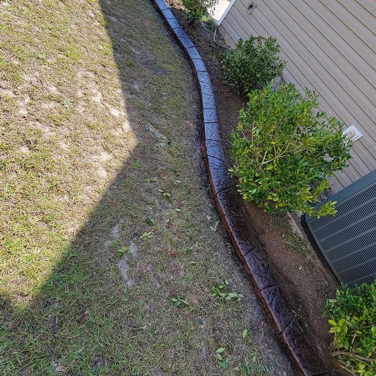 Stamped concrete curb running beside shrubs along gray siding