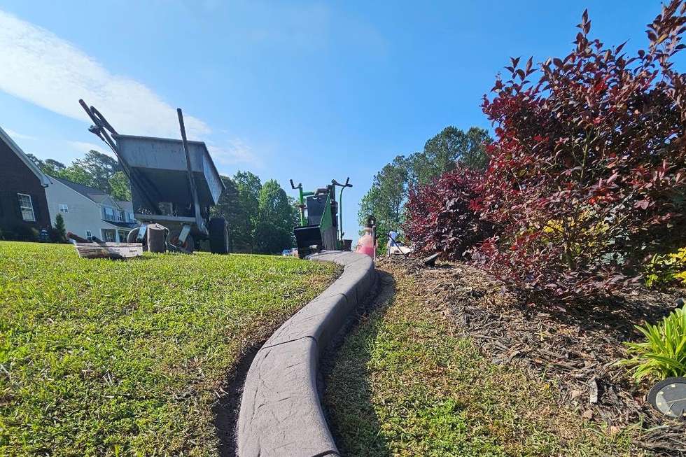 A long, continuous run of charcoal stamped concrete curbing sweeping along a residential lawn in Fayetteville, North Carolina